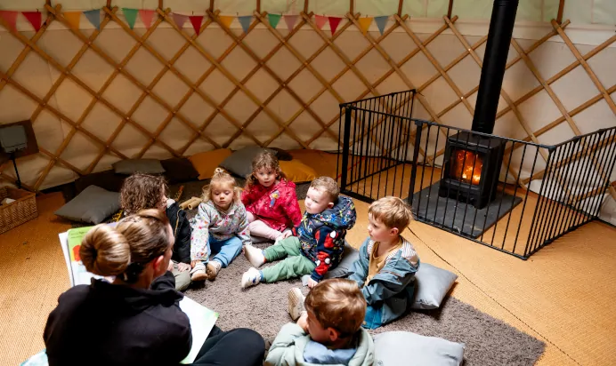 Key worker reading book to children in a bright tent at Kiddi Caru Day Nursery Preschool Torquay