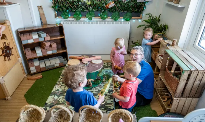 Key worker sat playing with with children and dinosaurs inside at Kiddi Caru Day Nursery Preschool Abington Park Northampton