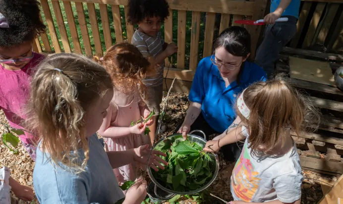 Key worker showing children leaves at Kiddi Caru Day Nursery Preschool Walnut Tree Milton Keynes