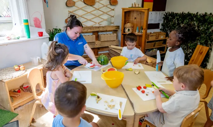 Key worker teaching children how to cut fruit at Kiddi Caru Day Nursery Preschool Abington Park Northampton
