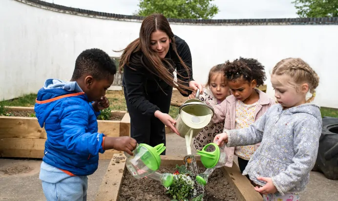 Key worker watering plants with children at Kiddi Caru Day Nursery Preschool Peterborough