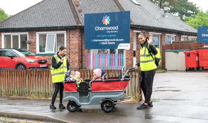 Key worker waving to the camera with children in a buggy at Charnwood Day Nursery Preschool Shepshed Loughborough