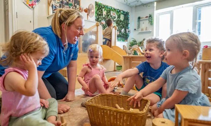 Key worker with children playing with wooden blocks at Kiddi Caru Day Nursery Preschool Abington Park Northampton