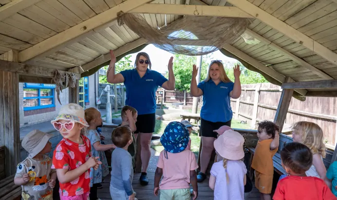 Key workers playing with children in wooden hut at Kiddi Caru Day Nursery Preschool Wellingborough