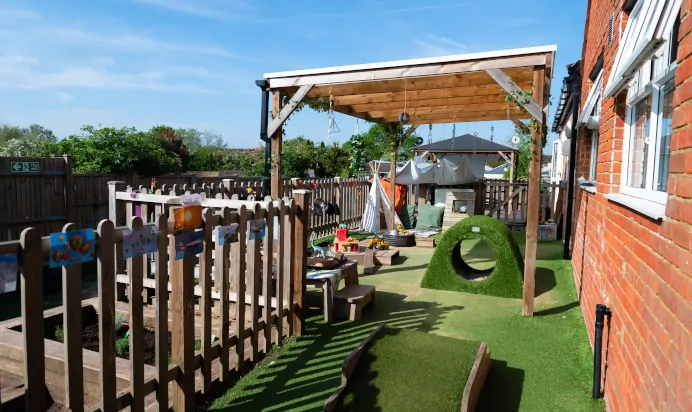 Outdoor play area with grass tunnel at Kiddi Caru Day Nursery Preschool Leighton Buzzard