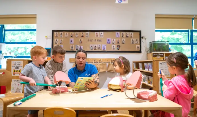 Small children reading book with key worker inside ineteractive space at Kiddi Caru Day Nursery Preschool Torquay