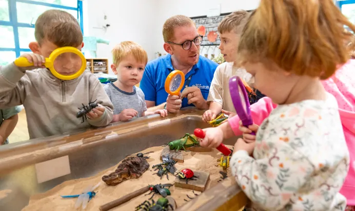 Small children using magnifying glass to look at toy bugs at Kiddi Caru Day Nursery Preschool Torquay