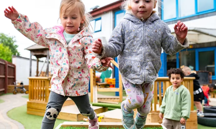 Two children jumping together at Kiddi Caru Day Nursery Preschool Peterborough