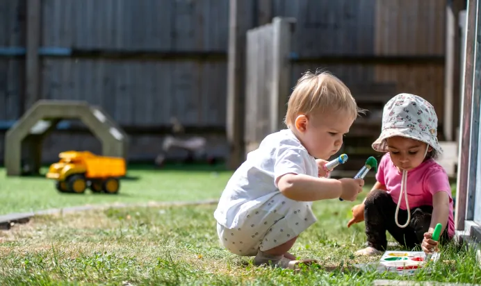 Two children playing with paint outside at Kiddi Caru Day Nursery Preschool Abington Park Northampton