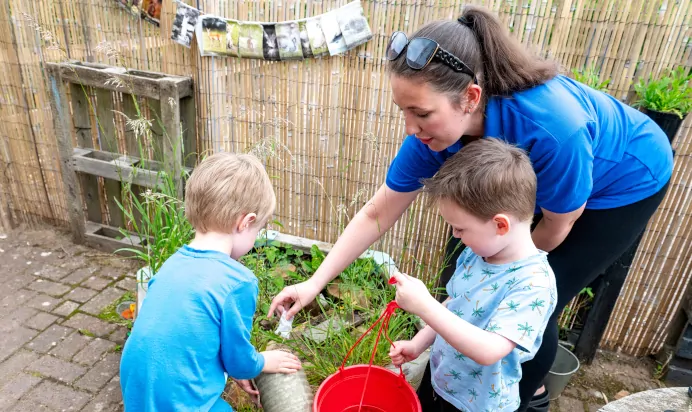 Two children water plants with key worker at Kiddi Caru Day Nursery Preschool Market Harborough
