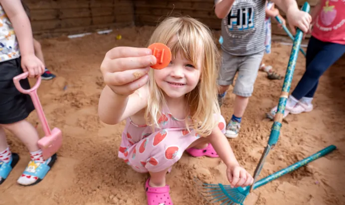 Child showing a toy to camera in sand pit at Kiddi Caru Day Nursery Preschool Fareham