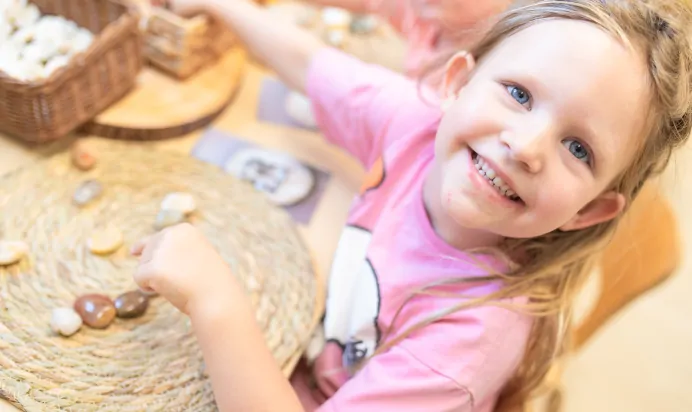 Child smiling whilst playing with stones at Kiddi Caru Day Nursery Preschool Market Ower
