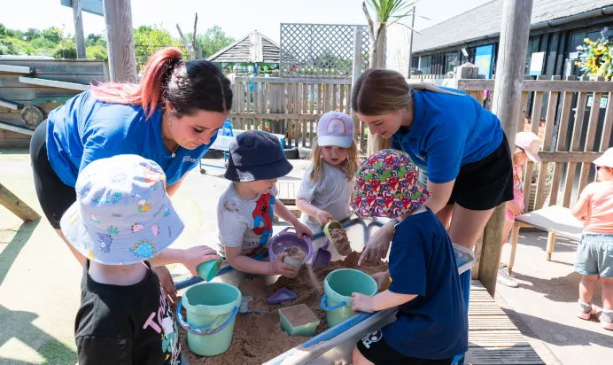 Children playing in sand pit with help from key workers at Kiddi Caru Day Nursery Preschool Market Ower