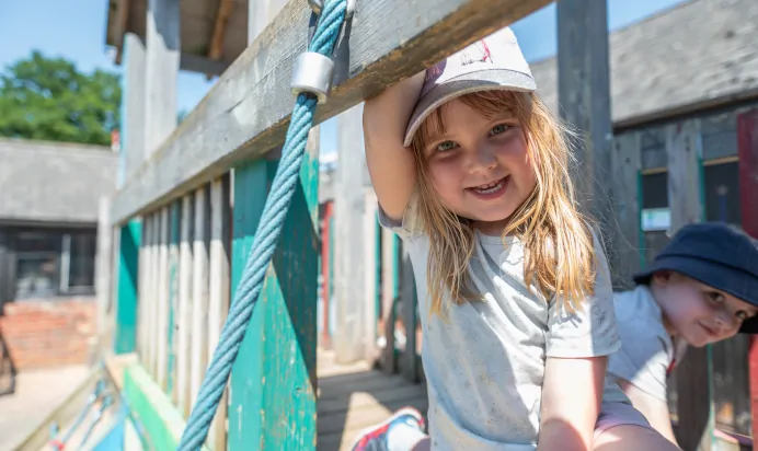 Children playing on climbing frame smiling at Kiddi Caru Day Nursery Preschool Market Ower