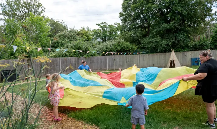 Children playing with colourful parachute in the garden at Kiddi Caru Day Nursery Preschool Fareham