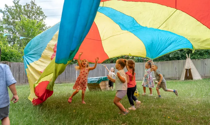 Children running under parachute at Kiddi Caru Day Nursery Preschool Fareham