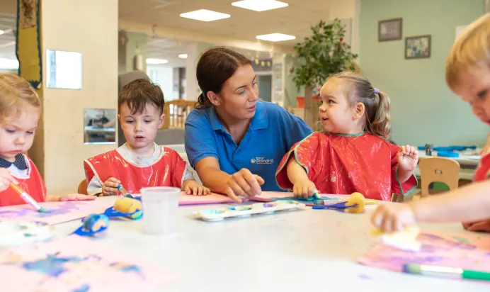 Children with key worker painting with sponges and brushes at Kiddi Caru Day Nursery Preschool Fareham