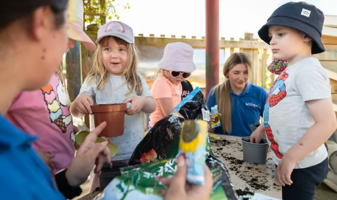 Key worker helping children plant sunflower seeds at Kiddi Caru Day Nursery Preschool Market Ower