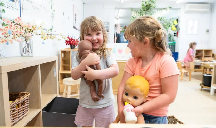 Two children playing with toy babies at Kiddi Caru Day Nursery Preschool Market Ower