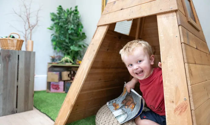 Child laughing in wooden teepee at Dicky Birds Nursery Preschool Pelham Road Wimbledon London