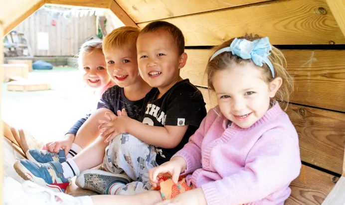 Children sitting in wooden tunnel at Dicky Birds Nursery Preschool Queens Road Wimbledon London