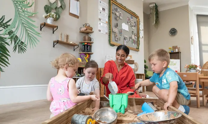 Key worker and children playing with sand pit at Dicky Birds Nursery Preschool Pelham Road Wimbledon London