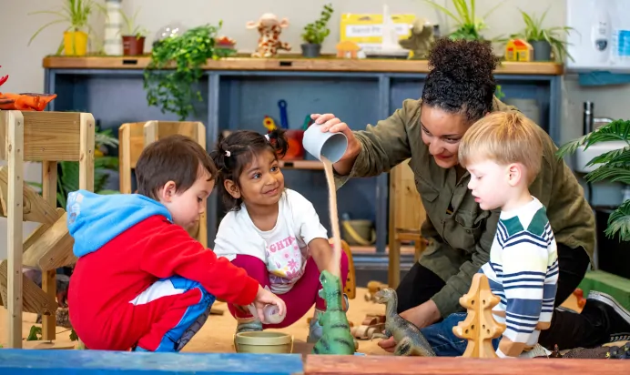 Key worker playing with children in sand pit at Dicky Birds Nursery Preschool Claremont Road Surbiton