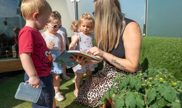 Key worker reading book to children at Dicky Birds Nursery Preschool Pelham Road Wimbledon London