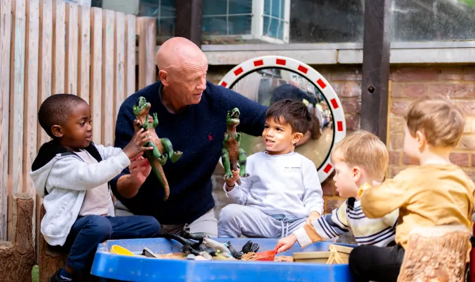 Key worker playing with children in sand pit at Dicky Birds Nursery Preschool Claremont Road Surbiton