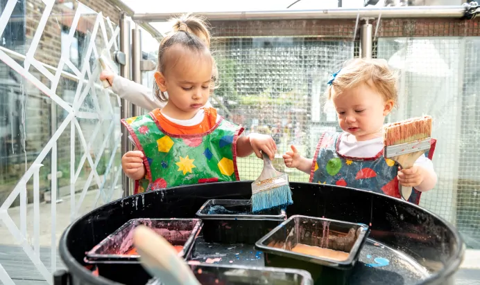 Two children playing with paint outside at Dicky Birds Nursery Preschool Queens Road Wimbledon London
