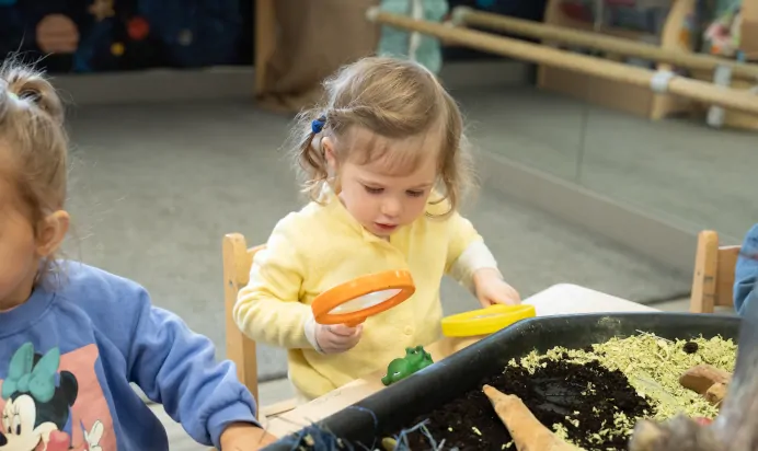 Child looking through magnifying glass at The Winchmore Hill Day Nursery London