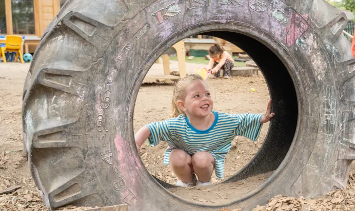 Child smiling in tyre at The Chingford Forest Day Nursery Preschool London