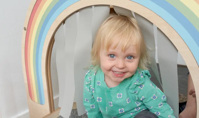 Child smiling while playing under rainbow at The Penge East Day Nursery Preschool London