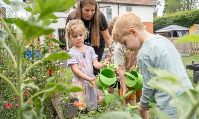 Children watering plants outside with key worker at The Daydream Nursery Preschool Woking
