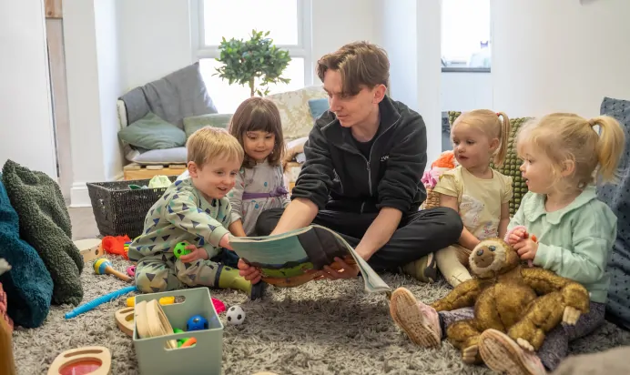 Keyworker and children reading book inside at The Ryan House Day Nursery Preschool Nottingham