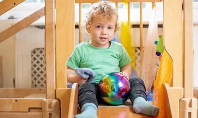 Child sitting on wooden slide at The Wishing Tree Nursery Preschool Brighton