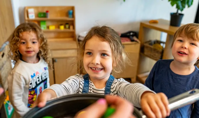 Children showing a key worker what they've made in the play kitchen at Kiddi Caru Day Nursery Preschool Crews Hole Bristol