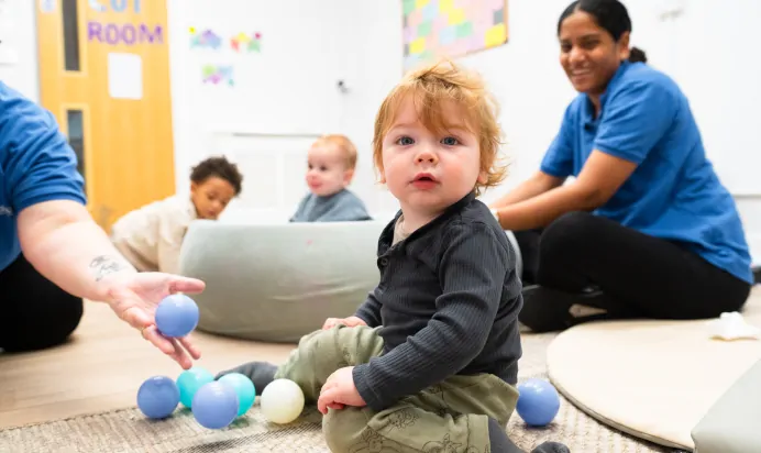 Child looking to camera playing with balls and key workers at Kiddi Caru Day Nursery Preschool Brislington Bristol