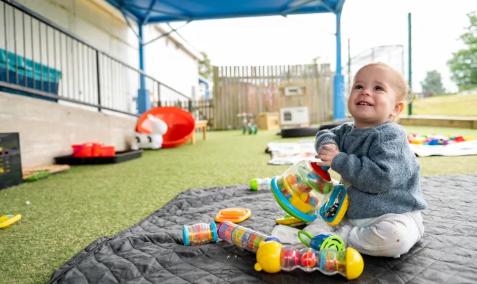 Child smiling whilst playing outside at Kiddi Caru Day Nursery Preschool Brislington Bristol