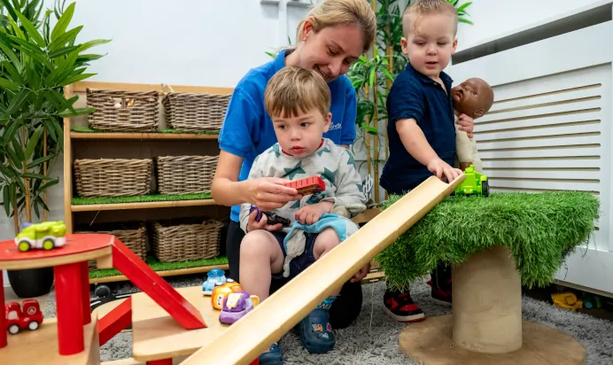 Children playing with cars and babies with key worker at Kiddi Caru Day Nursery Preschool Brislington Bristol