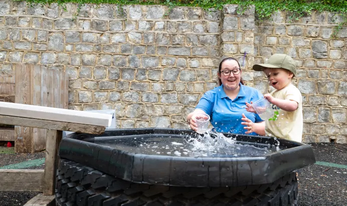 Key worker and child playing with water outdoors at Kiddi Caru Day Nursery Preschool Crews Hole Bristol