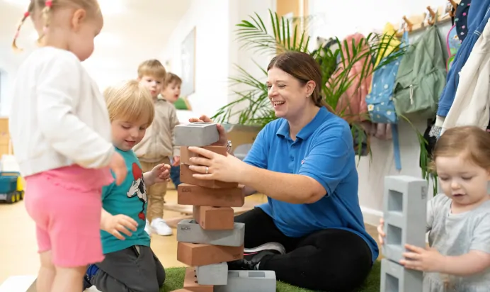 Key worker building a tower of foam bricks with children at Kiddi Caru Day Nursery Preschool Coronation Road Downend Bristol