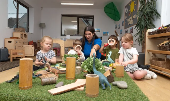 Key worker pointing to dinosaur with children at Kiddi Caru Day Nursery Preschool Coronation Road Downend Bristol