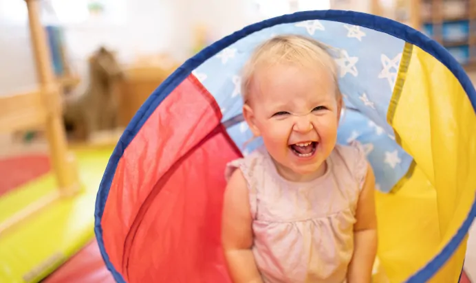Child laughing in rainbow tunnel at The Elan Day Nursery Haywards Heath