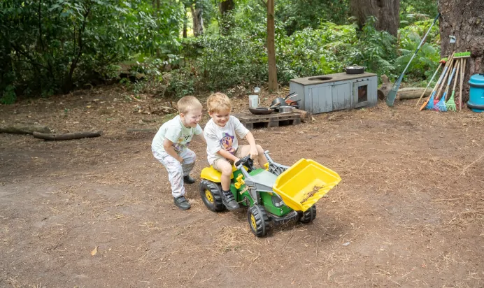 Child pushing friend on toy truck in the woods at The Puddleduck Preschool Priory Road Ascot