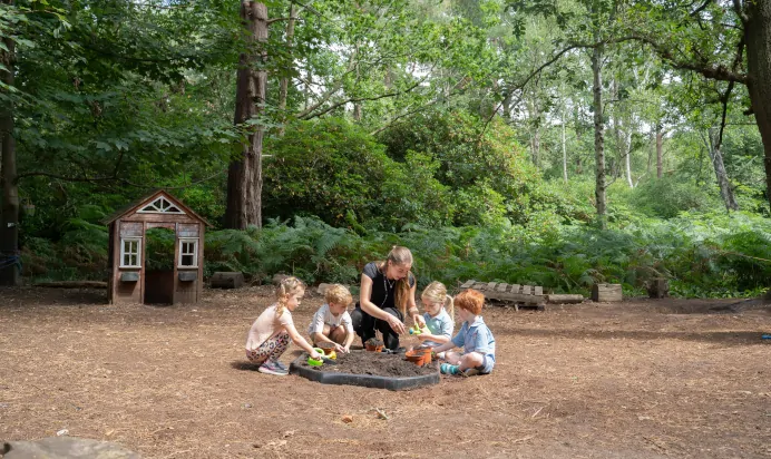 Children playing together in woods with key worker at The Puddleduck Preschool Priory Road Ascot