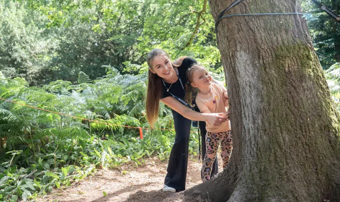 Key worker and child hiding behind tree smiling at The Puddleduck Preschool Priory Road Ascot