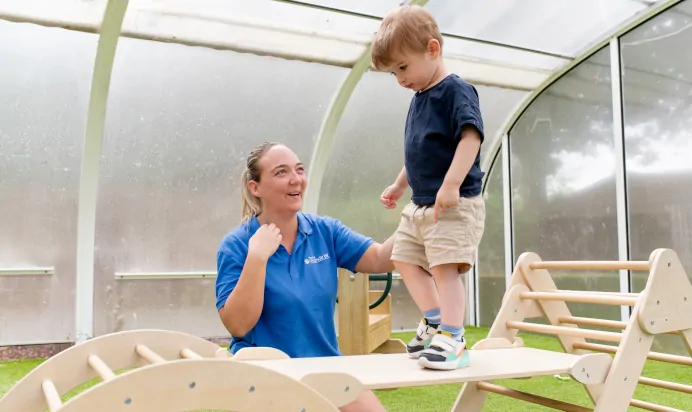 Key worker supporting child across play bridge at The College Town Montessori Nursery Preschool Sandhurst