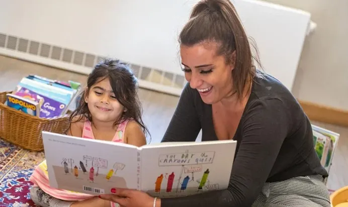 Adult reading a book to a child with a basket of books nearby.