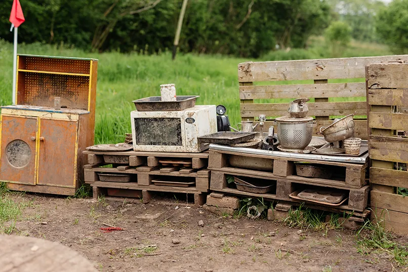 Outdoor rustic kitchen setup with old appliances and utensils on wooden pallets.